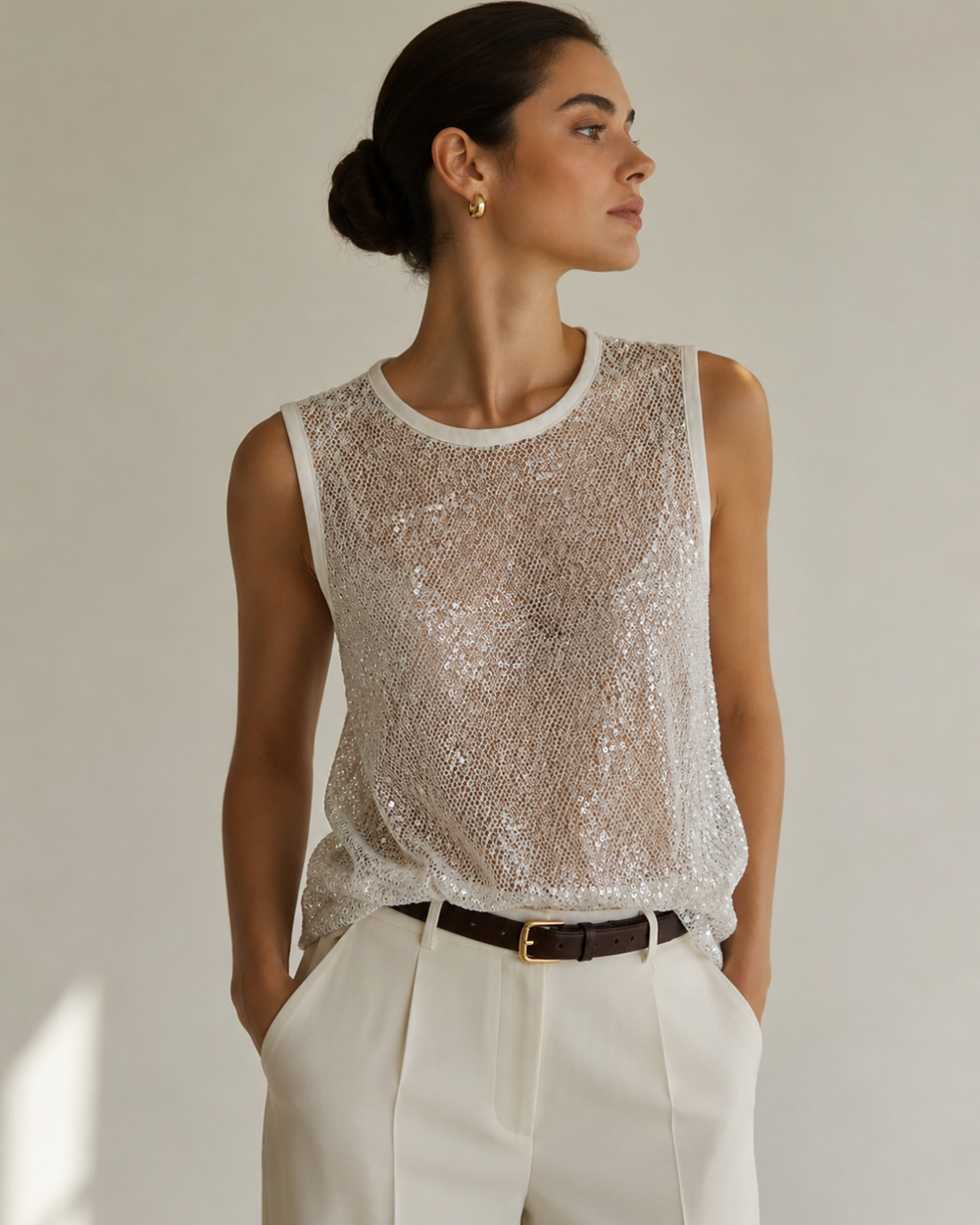 Blusa femenina en maya bordada con lentejuelas color blanco, diseño semitransparente sin mangas y cuello redondo. Estilo elegante y sofisticado para ocasiones especiales.