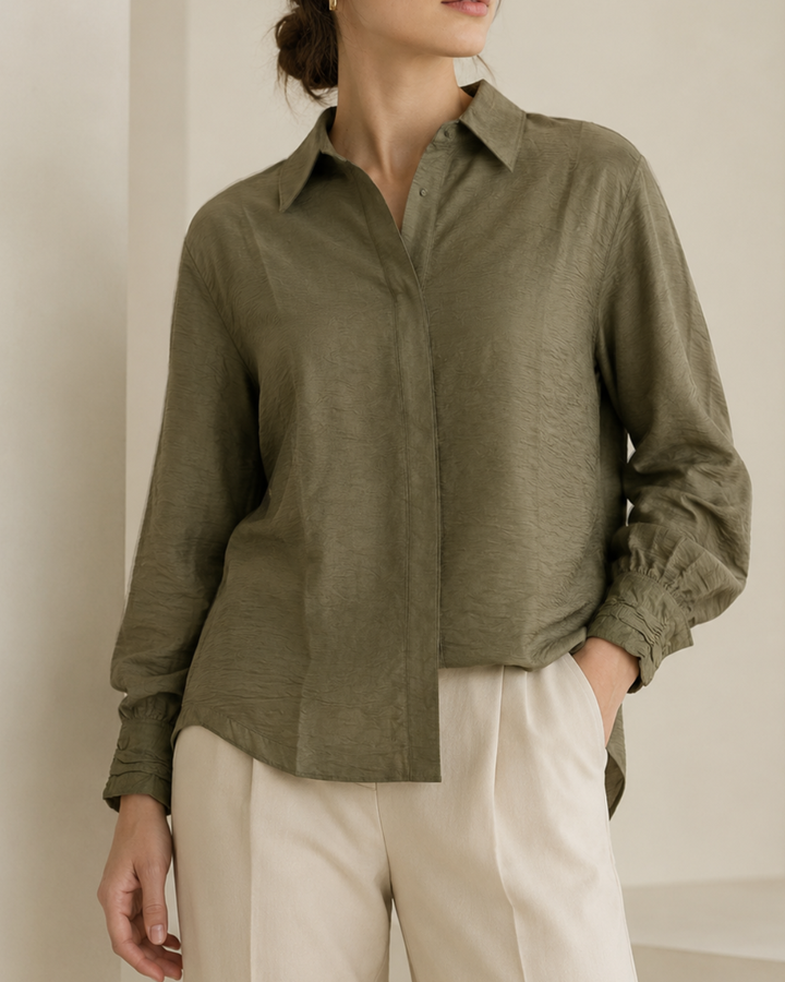 – Camisa de horma amplia
– Tela ligera, fluida y texturizada
– Composición: 85% viscosa, 15% nylon
– Cuello camisero clásico
– Botones ocultos con tapeta frontal
– Puños con diseño recogido
– Manga larga con volumen sutil
– Espalda con pieza superior y pliegue central
– Largo cómodo con caída natural
– Ideal para looks elegantes, casuales o de oficina