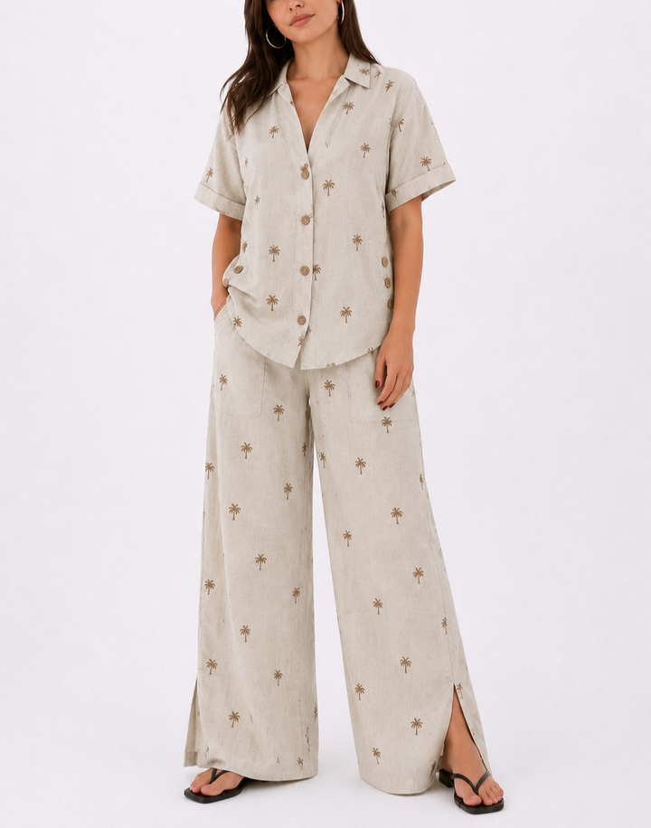 Blusa de manga corta
Cuello clásico
Botones frontales
Detalle de botones laterales decorativos
Pantalón de pierna amplia
Bolsillos de parche
Abertura lateral en la bota
Estampado sutil de palmeras
Tela fresca y de excelente caída