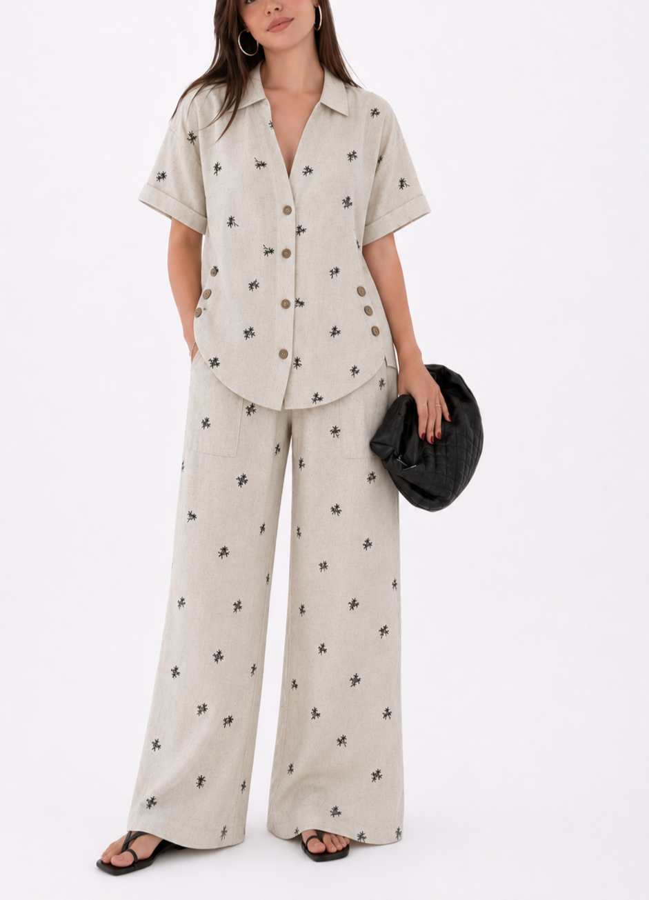 Blusa de manga corta
Cuello clásico
Botones frontales
Detalle de botones laterales decorativos
Pantalón de pierna amplia
Bolsillos de parche
Abertura lateral en la bota
Estampado sutil de palmeras
Tela fresca y de excelente caída