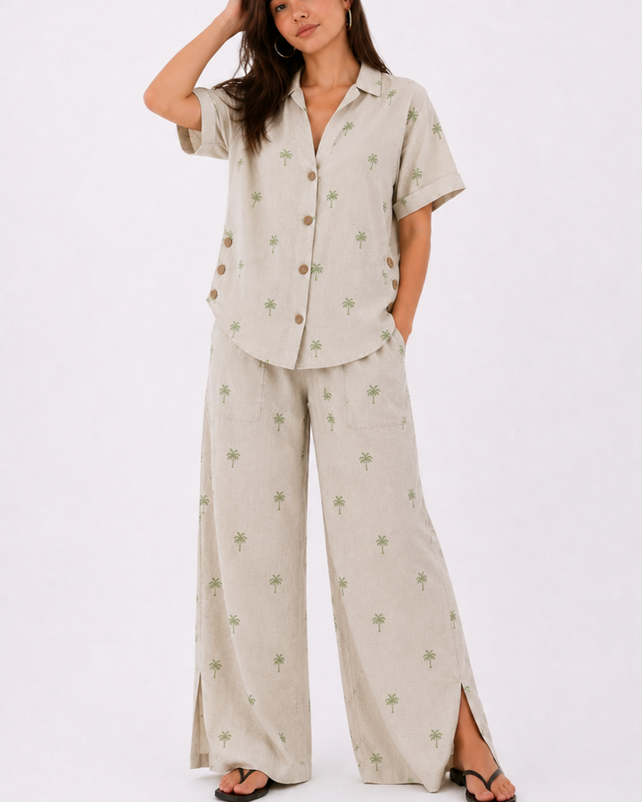 Blusa de manga corta
Cuello clásico
Botones frontales
Detalle de botones laterales decorativos
Pantalón de pierna amplia
Bolsillos de parche
Abertura lateral en la bota
Estampado sutil de palmeras
Tela fresca y de excelente caída